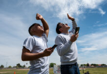 Two students shade their eyes as they watch a model rocket launch into the air at Maricopa Wells Middle School on March 28, 2024. [Bryan Mordt]